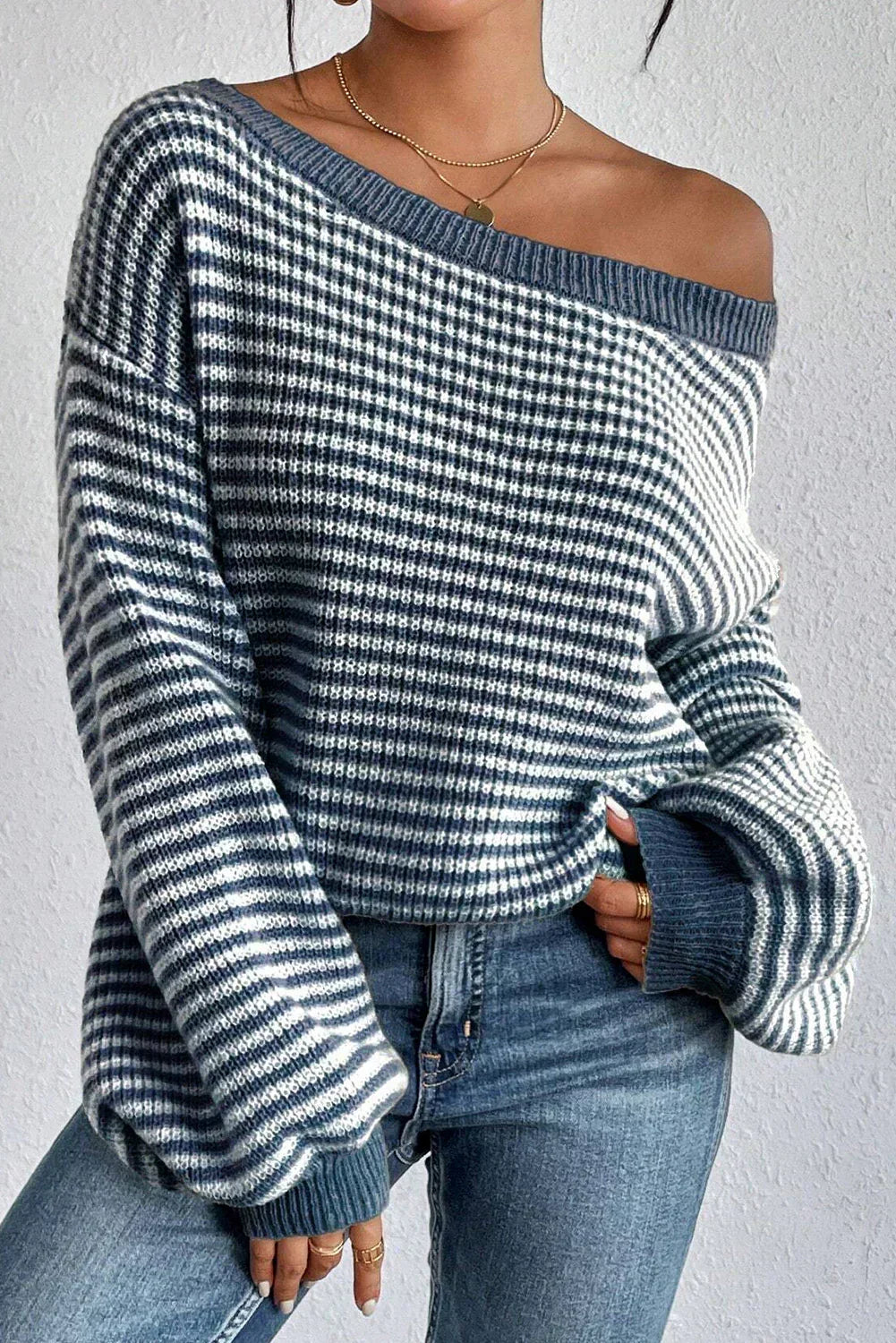 Woman wearing a striped off-shoulder knit sweater with voluminous sleeves, front view